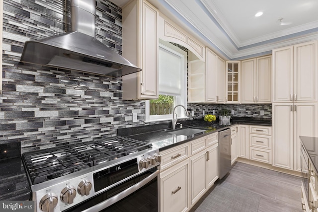 kitchen with cream cabinets, wall chimney range hood, sink, decorative backsplash, and appliances with stainless steel finishes