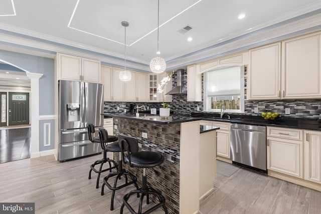 kitchen with a center island, cream cabinets, a kitchen breakfast bar, wall chimney range hood, and appliances with stainless steel finishes