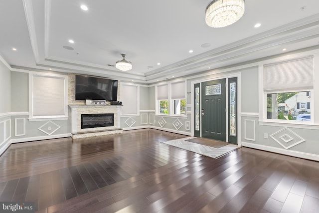 unfurnished living room featuring dark hardwood / wood-style flooring, a tray ceiling, crown molding, a notable chandelier, and a stone fireplace