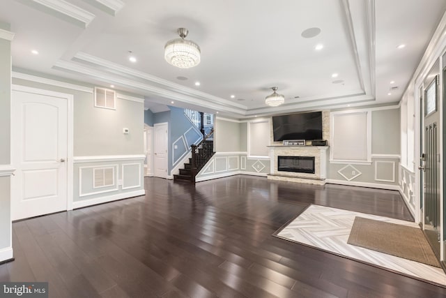 unfurnished living room with a tray ceiling, a stone fireplace, dark wood-type flooring, and a notable chandelier