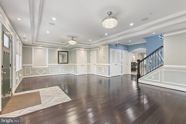 unfurnished living room featuring a tray ceiling, a chandelier, dark hardwood / wood-style floors, and ornamental molding