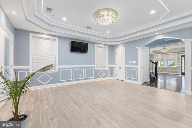 interior space with ornate columns, ornamental molding, a tray ceiling, light hardwood / wood-style flooring, and a notable chandelier