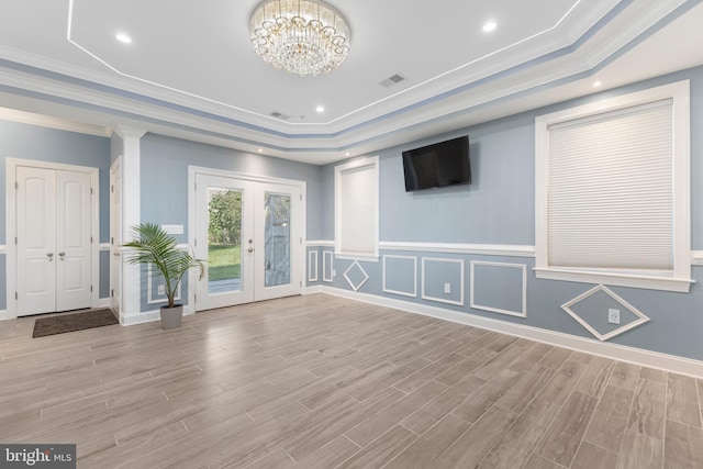 empty room with a tray ceiling, french doors, a chandelier, and ornamental molding