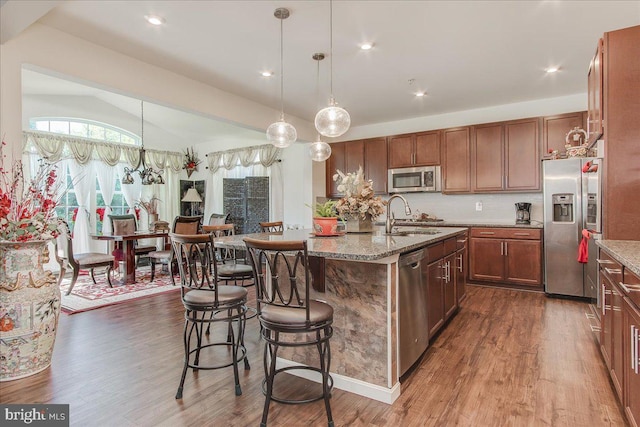 kitchen with sink, stainless steel appliances, decorative light fixtures, lofted ceiling, and a center island with sink