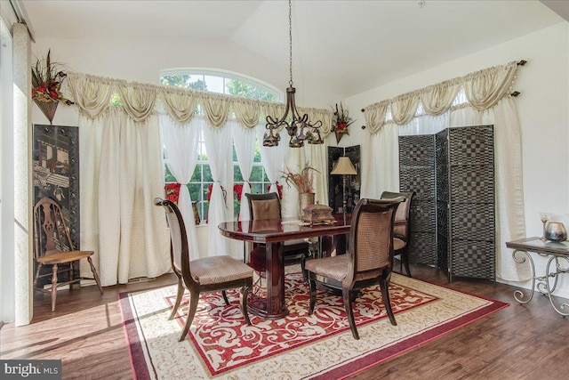 dining area featuring dark hardwood / wood-style floors, vaulted ceiling, and an inviting chandelier