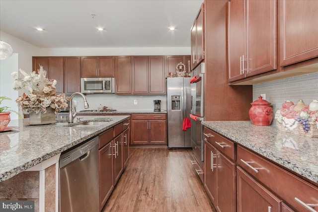 kitchen featuring sink, light hardwood / wood-style flooring, light stone countertops, appliances with stainless steel finishes, and tasteful backsplash