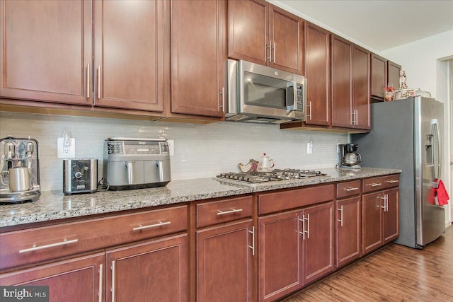 kitchen featuring tasteful backsplash, light stone countertops, light hardwood / wood-style floors, and appliances with stainless steel finishes