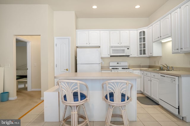 kitchen with white appliances, white cabinets, glass insert cabinets, light countertops, and a sink