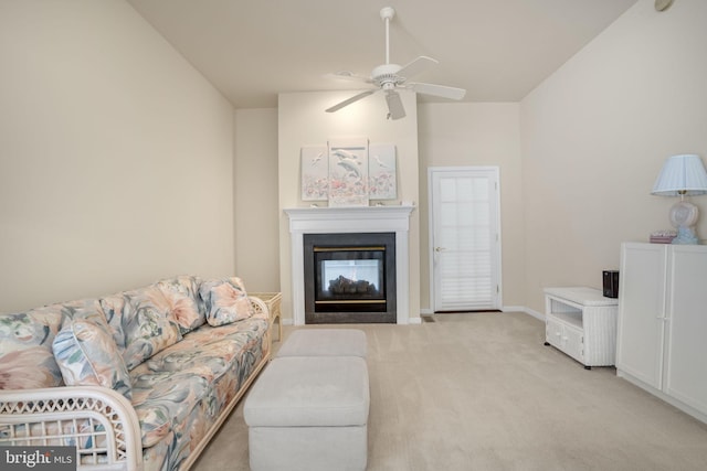 living area with ceiling fan, baseboards, a glass covered fireplace, and light colored carpet