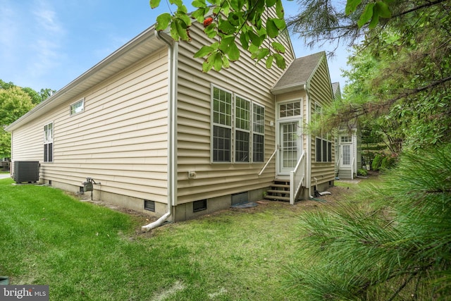 view of side of home featuring entry steps, central AC, and a yard