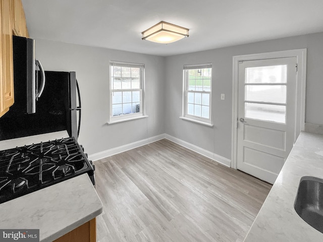 kitchen with black range with gas stovetop, light brown cabinetry, and light hardwood / wood-style flooring