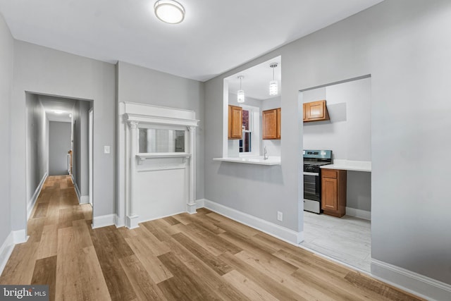 interior space with sink, light hardwood / wood-style floors, hanging light fixtures, and stainless steel range oven