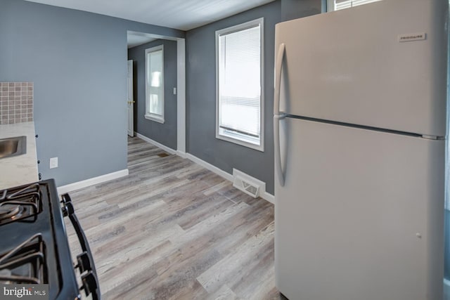 kitchen with black range oven, light wood-type flooring, and white refrigerator