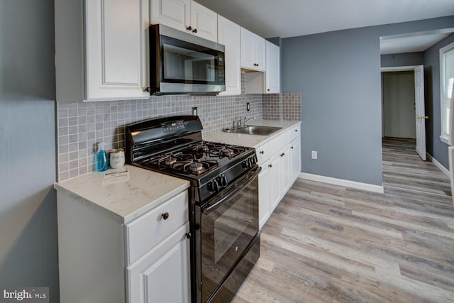 kitchen featuring black gas range, backsplash, sink, light stone countertops, and white cabinetry