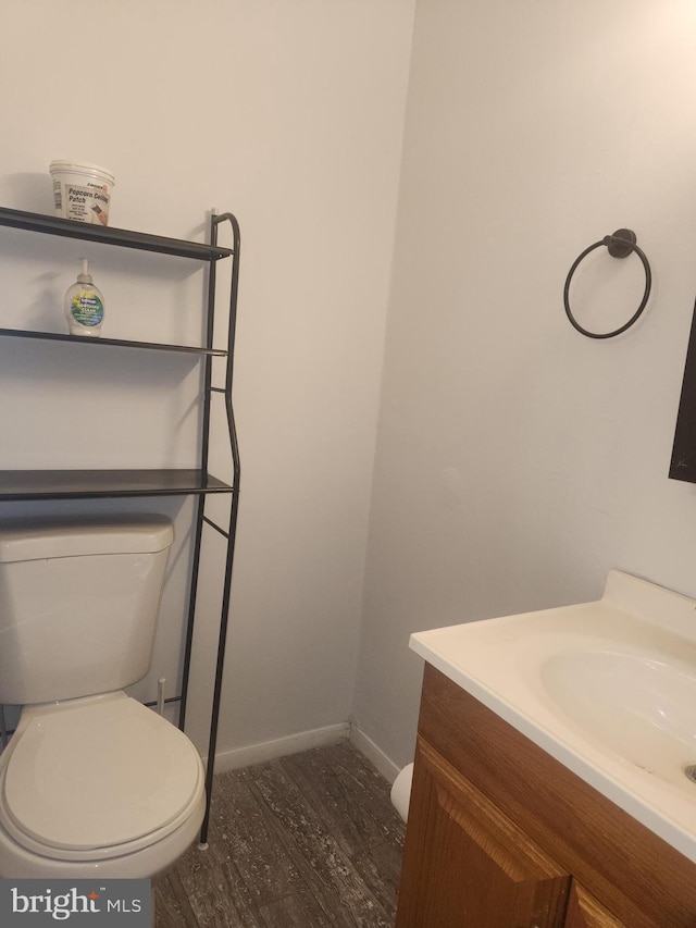 half bath featuring vanity, toilet, wood finished floors, and baseboards