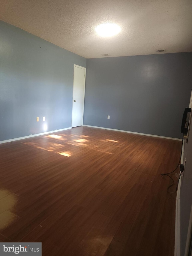 spare room featuring dark wood-style floors, visible vents, and baseboards