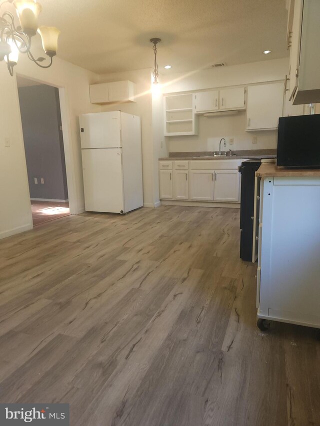 kitchen featuring freestanding refrigerator, wood finished floors, hanging light fixtures, white cabinets, and a sink