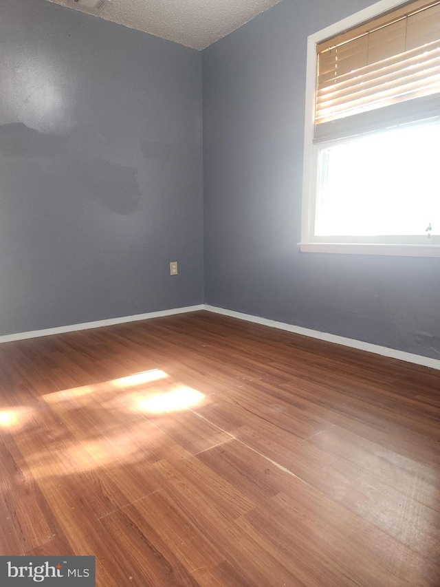 spare room featuring baseboards, a textured ceiling, and wood finished floors