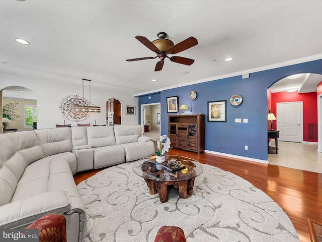 living room featuring crown molding, light hardwood / wood-style flooring, and ceiling fan with notable chandelier