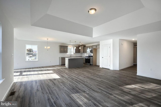 unfurnished living room with dark wood-type flooring, a tray ceiling, sink, and an inviting chandelier