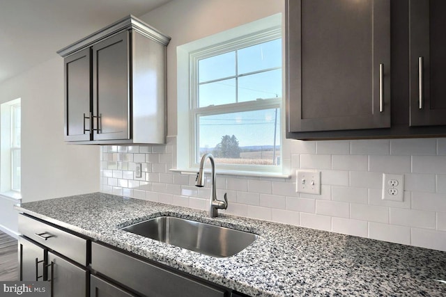 kitchen with tasteful backsplash, sink, light stone counters, and dark brown cabinetry