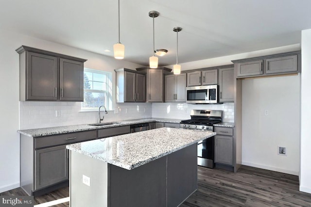 kitchen with light stone countertops, pendant lighting, a kitchen island, stainless steel appliances, and sink