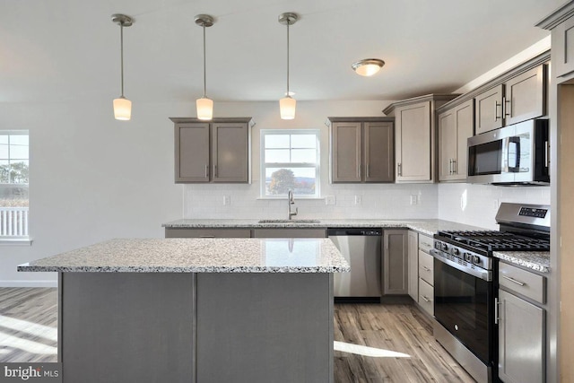 kitchen with light hardwood / wood-style floors, appliances with stainless steel finishes, decorative backsplash, decorative light fixtures, and sink