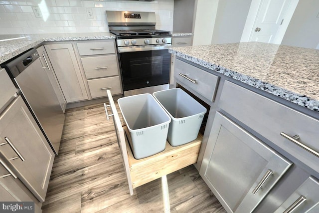 kitchen with decorative backsplash, appliances with stainless steel finishes, gray cabinets, and light hardwood / wood-style flooring