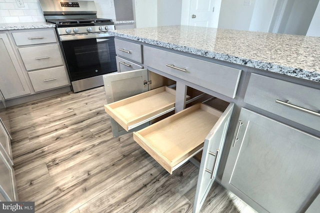 kitchen featuring light stone counters, gray cabinets, and stainless steel gas range oven