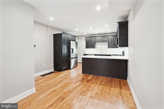 kitchen with tasteful backsplash, kitchen peninsula, stainless steel fridge, and light hardwood / wood-style flooring