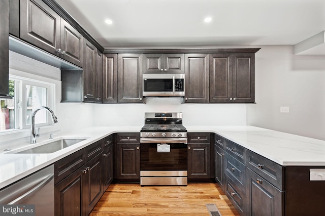 kitchen with sink, light hardwood / wood-style flooring, appliances with stainless steel finishes, light stone counters, and dark brown cabinetry