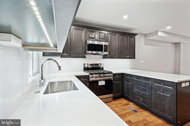 kitchen with kitchen peninsula, light wood-type flooring, dark brown cabinets, stainless steel appliances, and sink