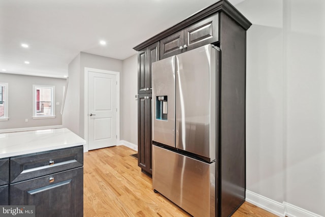 kitchen featuring dark brown cabinets, light hardwood / wood-style floors, light stone counters, and stainless steel fridge with ice dispenser