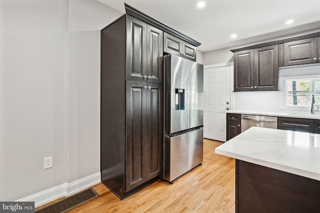 kitchen featuring light stone counters, dark brown cabinetry, stainless steel appliances, sink, and light hardwood / wood-style flooring