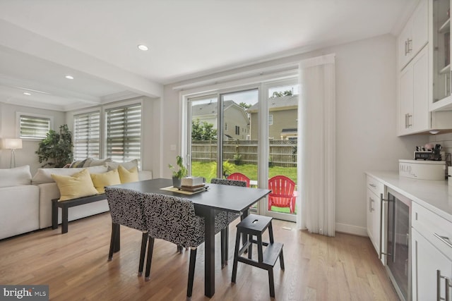 dining area with beam ceiling, wine cooler, and light hardwood / wood-style flooring