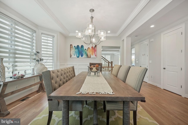 dining room with an inviting chandelier, ornamental molding, a tray ceiling, and light hardwood / wood-style flooring