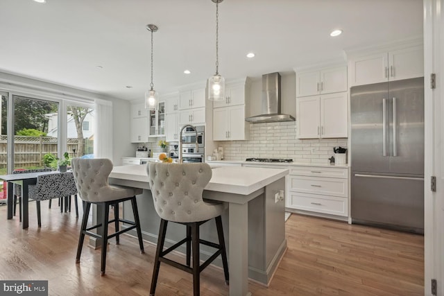 kitchen featuring white cabinets, wall chimney exhaust hood, an island with sink, and appliances with stainless steel finishes