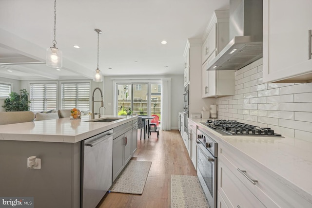 kitchen featuring wall chimney exhaust hood, stainless steel appliances, sink, white cabinets, and an island with sink