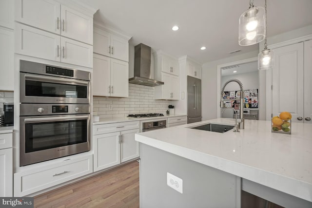 kitchen with white cabinets, wall chimney exhaust hood, tasteful backsplash, decorative light fixtures, and stainless steel appliances