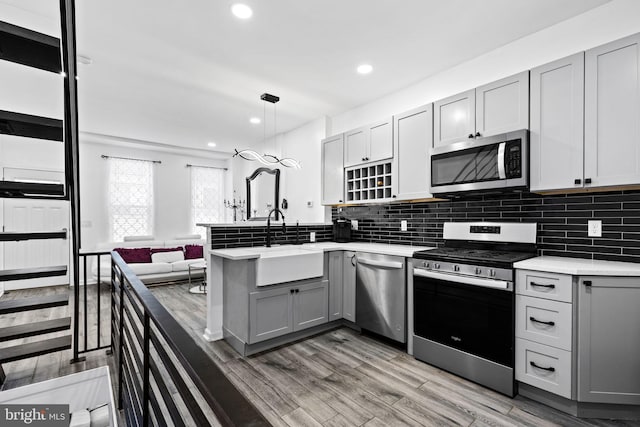 kitchen featuring kitchen peninsula, stainless steel appliances, sink, pendant lighting, and gray cabinets