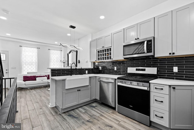 kitchen featuring kitchen peninsula, stainless steel appliances, sink, pendant lighting, and gray cabinets