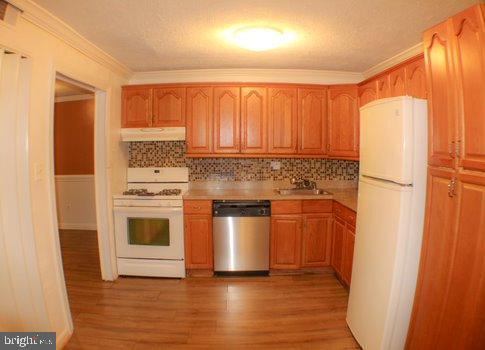 kitchen with decorative backsplash, ornamental molding, white appliances, sink, and light hardwood / wood-style floors