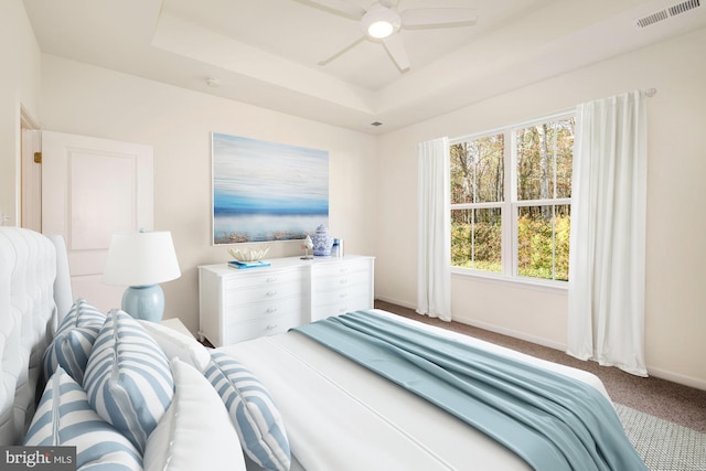 carpeted bedroom with a tray ceiling and ceiling fan