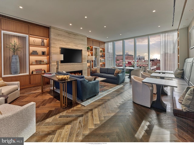 living room with a fireplace, dark parquet floors, built in features, and a wall of windows