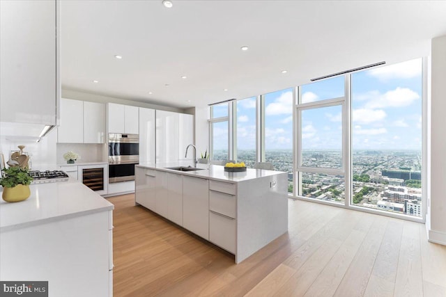 kitchen with white cabinetry, a center island with sink, sink, and a wall of windows