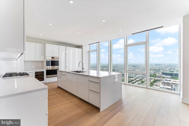 kitchen featuring expansive windows, a center island with sink, white cabinets, and sink