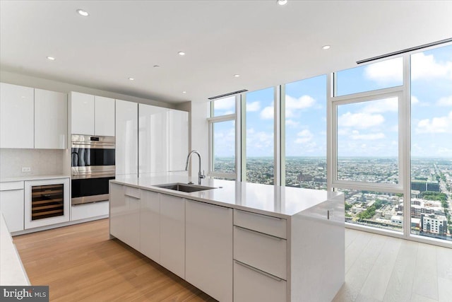 kitchen featuring sink, beverage cooler, expansive windows, double oven, and white cabinets