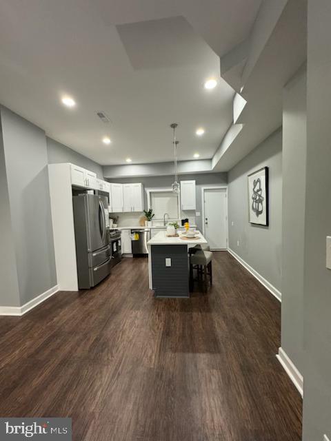 kitchen featuring a center island, dark wood-type flooring, white cabinets, hanging light fixtures, and appliances with stainless steel finishes