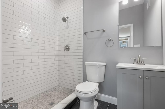 bathroom featuring tile patterned flooring, a tile shower, vanity, and toilet