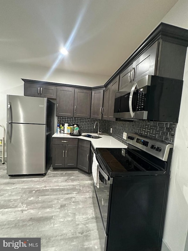 kitchen featuring sink, light hardwood / wood-style flooring, appliances with stainless steel finishes, tasteful backsplash, and dark brown cabinetry